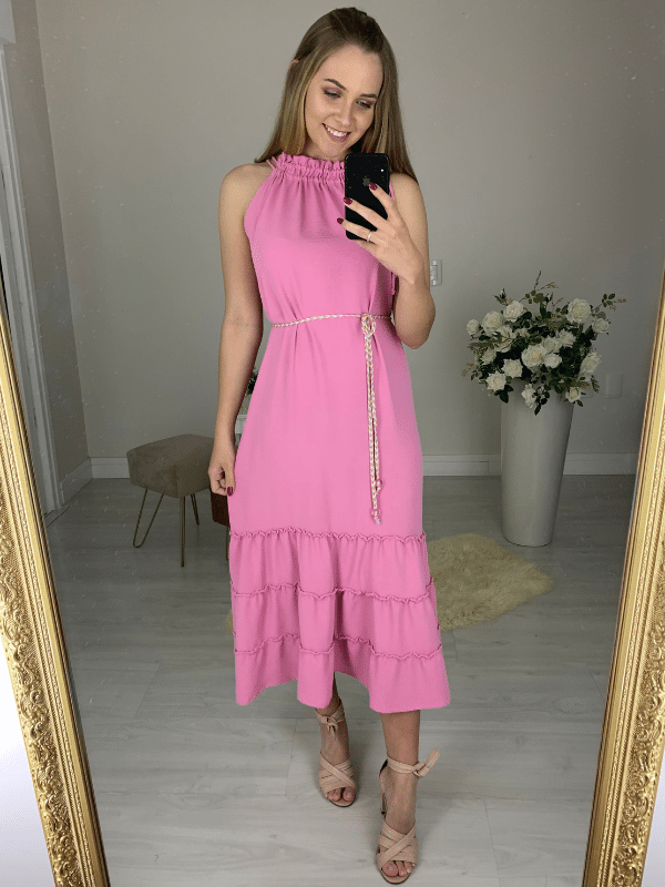 Vestido confeccionado em um tecido leve, fluido e que não amassa. Possui decote de amarração com detalhe franzido e dois cordões. Acompanha um cinto trançado das mesmas cores da peça. Sua saia tem comprimento midi e três babados. 
