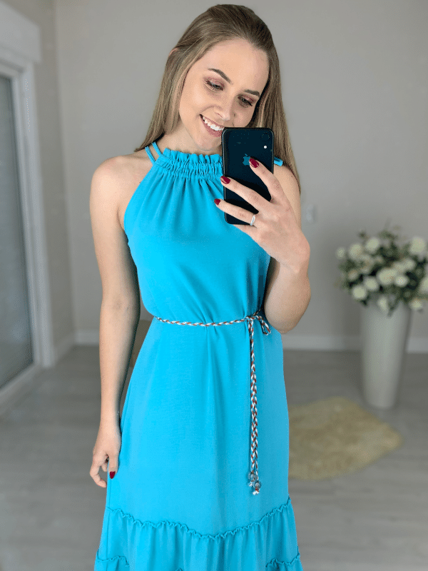 Vestido confeccionado em um tecido leve, fluido e que não amassa. Possui decote de amarração com detalhe franzido e dois cordões. Acompanha um cinto trançado das mesmas cores da peça. Sua saia tem comprimento midi e três babados. 